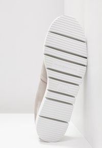 Baskets en suède gris avec une épaisse semelle en caoutchouc blanc. Présentent des rainures horizontales et un logo embossé sur le talon. Design épuré et minimaliste.