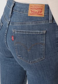 Dark blue denim jeans with a mid-rise fit, featuring a leather patch at the back waist and a small red Levi's tab on the back pocket.
