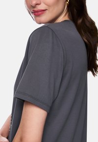 Graues T-Shirt mit kurzen Ärmeln und entspanntem Sitz, mit rundem Ausschnitt und weicher Textur. Sichtbare Nahtdetails an den Ärmeln.