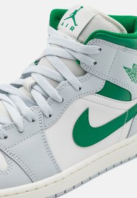 Høye sneakers i lys grå lær med grønne detaljer, med en grønn swoosh-logo og en polstret grønn innside. Hvite snører og mellomsåle.