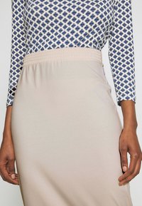 Béžová sukně s elastickým pasem, doplněná dlouhým rukávem s potiskem modrých květin na bílém pozadí.