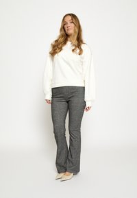 Biela mikina s balónovými rukávmi, skombinovaná so sivými rozšírenými nohavicami s jemným vzorom. Outfit dopĺňajú béžové topánky s špicatou špičkou.