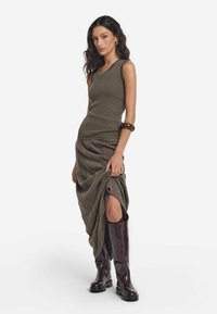 Olivgrön ribbad linne i kombination med en strukturerad brun kjol med en sidoverskärning, kompletterad med knähöga glansiga bordeauxstövlar.