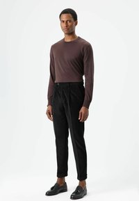 Bruine longsleeve gecombineerd met zwarte corduroy broek. Schoenen zijn zwarte loafers met een decoratieve kwast.