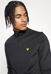 Zwarte pullover met rits van gladde stof, met een subtiele gouden arend logo op de borst en een gestroomlijnd pasvorm.