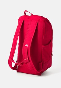 Red backpack featuring padded, mesh straps, a top handle, and a side pocket. Zip closure and reinforced stitching for durability.