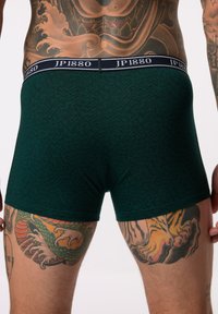 Boxer shorts verts à motif avec une taille sombre étiquetée "JP1880". Ils présentent une texture en chevrons et un ajustement près du corps.