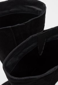 Botines de ante negro con tejido suave y texturizado, que presentan una apertura redondeada y laterales flexibles para facilitar el uso.