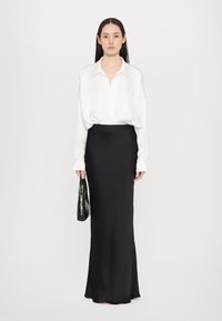 White, long-sleeve blouse paired with a black, floor-length skirt. A black, croc-embossed handbag is held in one hand. Smooth fabric texture.