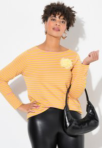 Maglietta a maniche lunghe con righe orizzontali gialle e rosa, decorata con un'applicazione a forma di fiore giallo. Borsa a tracolla in pelle nera con una forma curvata.