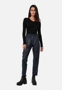 Haut noir à rayures, manches longues, assorti à un jogging en cuir synthétique bleu foncé, avec une taille élastique et une coupe à la cheville. Bottes noires massives.