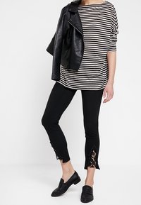 Svart läderbikerjacka, randig långärmad topp, svarta cropped byxor med spetsdekoration, och svarta loafers. Avslappnad, lager-på-lager-look.