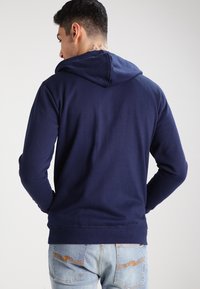 Marineblauwe hoodie met lange mouwen, zachte stof en een kangoeroezak aan de voorkant. Ribgebreide boorden en zoom.