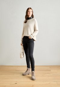 Beżowy sweter w prążki, czarne legginsy, taupe'owe buty na sznurówki i kremowa torebka. Gładkie faktury, luźny krój i neutralna paleta kolorów.