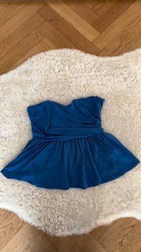 Blue strapless dress with gathered waist and flared skirt laid flat on a cream fluffy rug over wooden parquet floor.