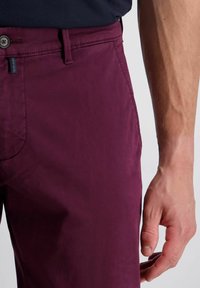 Bordeauxkleurige lichtgewicht broek met een gladde textuur. Voorzien van een knoopsluiting, een zijzak en gedetailleerde stiksels op de tailleband.