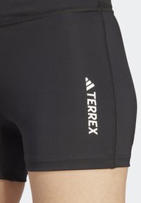 Lähikuva mustista urheiluhousuista, joissa on valkoinen "TERREX"-logo vasemmassa reidessä ja näkyvät ommellut saumat.