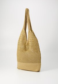 Sac fourre-tout en paille tissée de couleur beige chaud. Il possède deux longues poignées, une forme décontractée et une surface texturée avec un design en tissage ouvert.