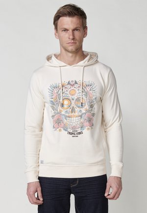 Crème hoodie met een kleurrijke schedelafbeelding, bloemaccenten en de tekst "Tropic Vibes." Voorzien van een trekkoordkap en ribgebreide manchetten.