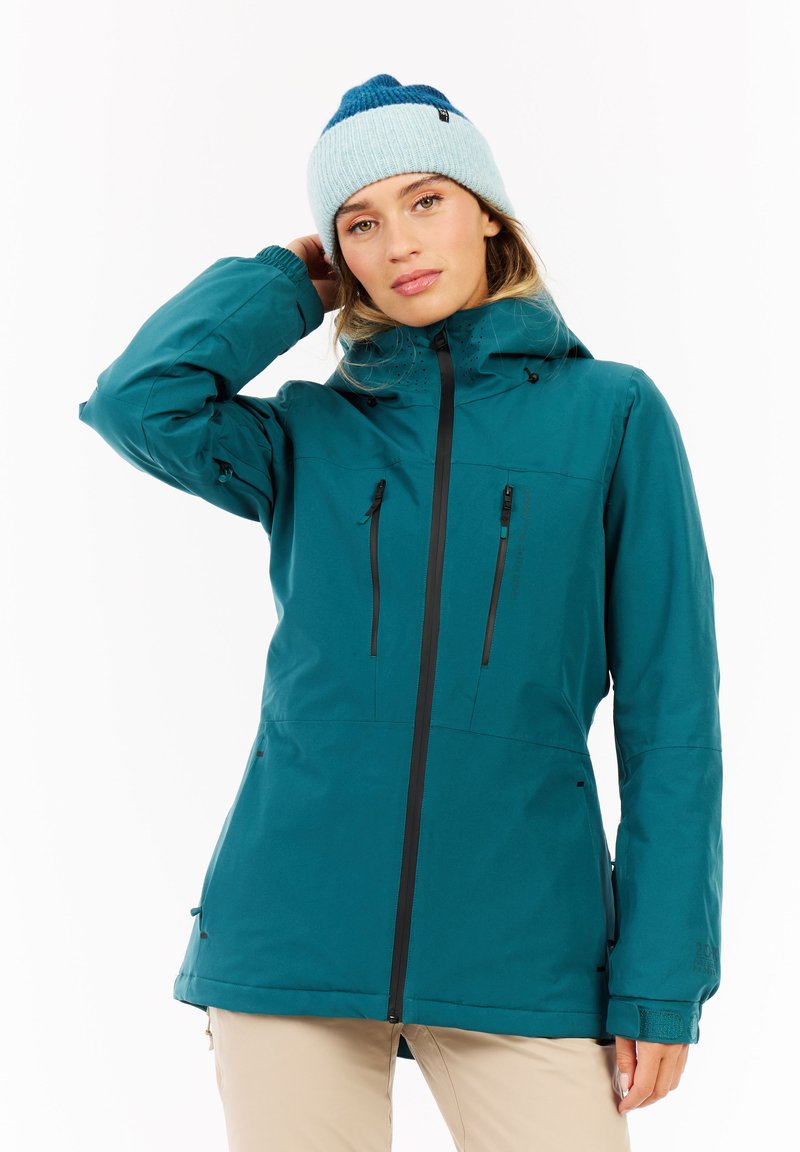 Türkisfarbende wasserdichte Jacke mit einem Frontreißverschluss, schwarzen Akzenten und mehreren Taschen. Gerippte blaue Strickmütze, die den Farbhervorhebung betont.