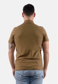 Polo shirt marrone a maniche corte, design attillato, texture liscia, con due spacco laterali all'orlo, indossato con jeans azzurri strappati.