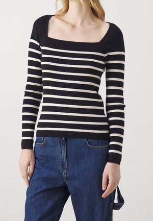 Persona con una camiseta de manga larga a rayas horizontales en blanco y negro, con escote cuadrado y jeans de mezclilla azul.