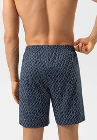 Navy zwembroek met een wit herhalend berenpatroon, elastische tailleband en knielange snit. Het stof voelt glad en licht aan.