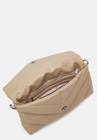 Beżowa miękka skórzana torebka na ramię z klapką i wewnętrzną kieszenią na zamek, pokazana otwarta na białym tle.
