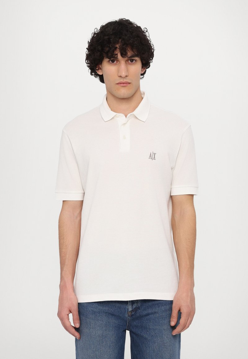 Lys beige polo skjorte lavet af bomuld, med klassisk krave, korte ærmer og et lille logo på venstre bryst. Bæres med blå jeans.