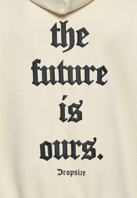 Cremefarbener Hoodie mit großen schwarzen gotischen Buchstaben, die "die Zukunft gehört uns" lesen. Enthält den Markennamen "Dropsize" in kleinerer Schrift.