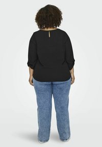 Blusa nera, comoda e larga, con maniche a tre quarti, dotata di un dettaglio a chiave sul retro. Abbinata a jeans azzurri a gamba dritta.