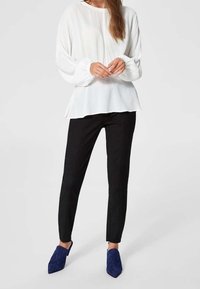 Weißes Langarmoberteil mit weit ausgestellten Ärmeln, kombiniert mit schwarzen Slim-Fit-Hosen und blauen Wildleder-Pumps mit spitzem Fuß. Einfaches, modernes Design.