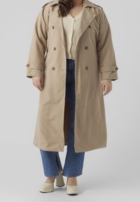 Beige trenchcoat met dubbelzijdige knopen en grote revers. Draag het over een crème trui en blauwe high-waisted jeans. Stevige, lichtgekleurde hakken.