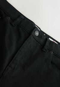 Black denim jeans featuring a smooth texture, metal button closure, and stitched pockets. The waistband has a contrasting inner pattern.