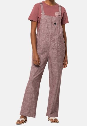 Persona vistiendo un mono texturizado color malva con tirantes ajustables sobre una camiseta de manga corta a juego y sandalias de dedo blancas.