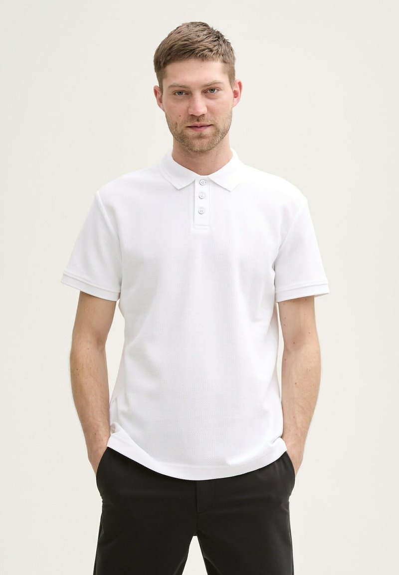 Witte polo in geweven stof met een drie-knopen placket en korte mouwen. Gecombineerd met donkere broek voor contrast.
