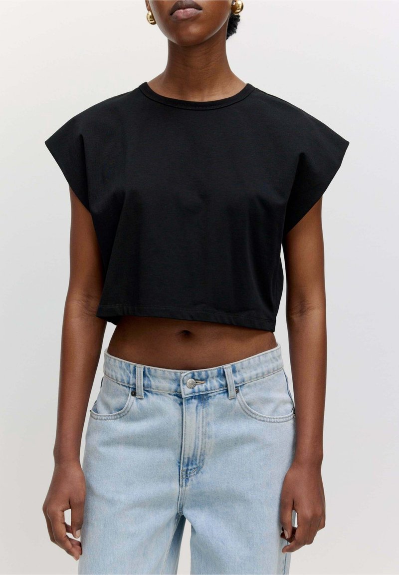 T-shirt noir court en coton avec manches courtes structurées, associé à un jean denim bleu clair taille haute avec fermeture à boutons.