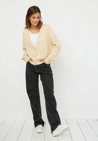 Beige knit cardigan with a V-neck and buttons, paired with black wide-leg jeans and white sneakers. The cardigan has ribbed cuffs and hem.