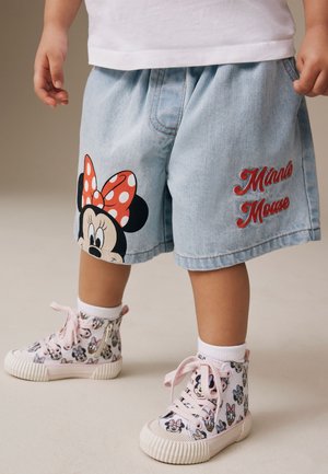 Barn iført lyseblå Minnie Mouse-shorts og hvide høje sneakers med lyserøde snørebånd og Minnie Mouse-ansigtsmønster.