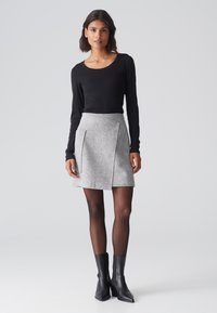 Schwarzes Langarmoberteil mit Rundhalsausschnitt, kombiniert mit einem grauen, strukturierten Rock mit schrägen Taschen und schwarzen Knöchelstiefeln.