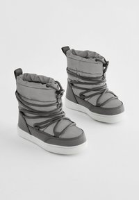 Grijze geïsoleerde laarzen met een ribbelontwerp, elastische veters en een gewatteerde kraag, met een witte rubberen zool. Geweven synthetisch materiaal.