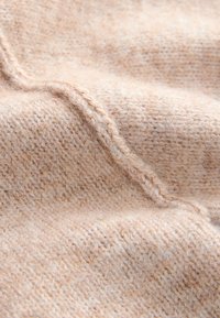 Bézs textília puha, texturált fonallal, látható varrásmintákkal és meleg, kötött megjelenéssel.