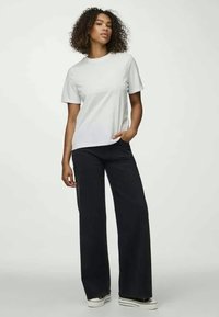 White crew-neck t-shirt and wide-leg black pants with a front pocket. Smooth fabric with a casual fit, featuring white sneakers.
