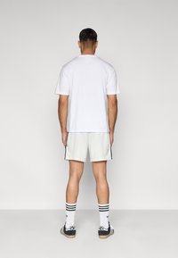 Camiseta blanca de manga corta combinada con pantalones cortos gris claro con rayas laterales, usada con calcetines a rayas blancos y negros y zapatillas negras.