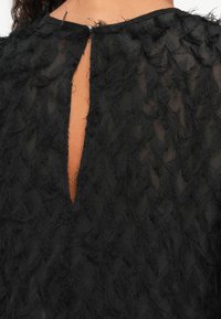 Schwarzes Kleid aus strukturiertem Stoff mit ausgefranstem, geschichtetem Detail, Öffnung am Schlüsselbein und glattem Rundhals.