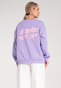 Fioletowy sweatshirt o luźnym kroju, z teksturowanym różowym napisem „SECONDO MECI STA” na plecach oraz ściągaczami na rękawach i u dołu.