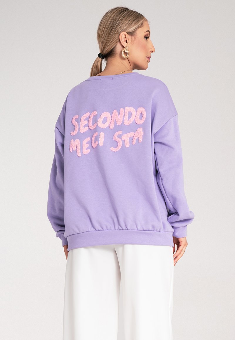 Fioletowy sweatshirt o luźnym kroju, z teksturowanym różowym napisem „SECONDO MECI STA” na plecach oraz ściągaczami na rękawach i u dołu.