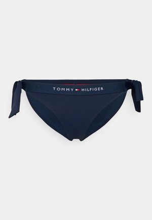 Bas de bikini bleu marine avec des accents à nouer sur les côtés, doté d'une bande logo avec "TOMMY HILFIGER" en blanc et rouge. Tissu lisse et extensible.