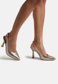 Zapatos de tacón slingback plateados metálicos con puntera puntiaguda, que presentan un diseño elegante, una pequeña hebilla y un tacón texturizado.