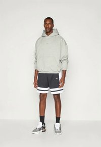 Šedá mikina s kapucí a přední kapsou, kombinovaná s černými šortkami se bílými pruhy a teniskami s texturovaným designem.